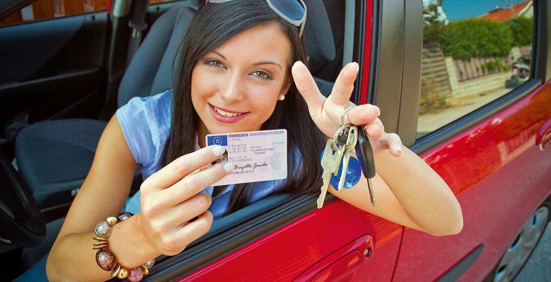 Junge Frau im Auto zeigt Ihren Führerschein und die Autoschlüssel